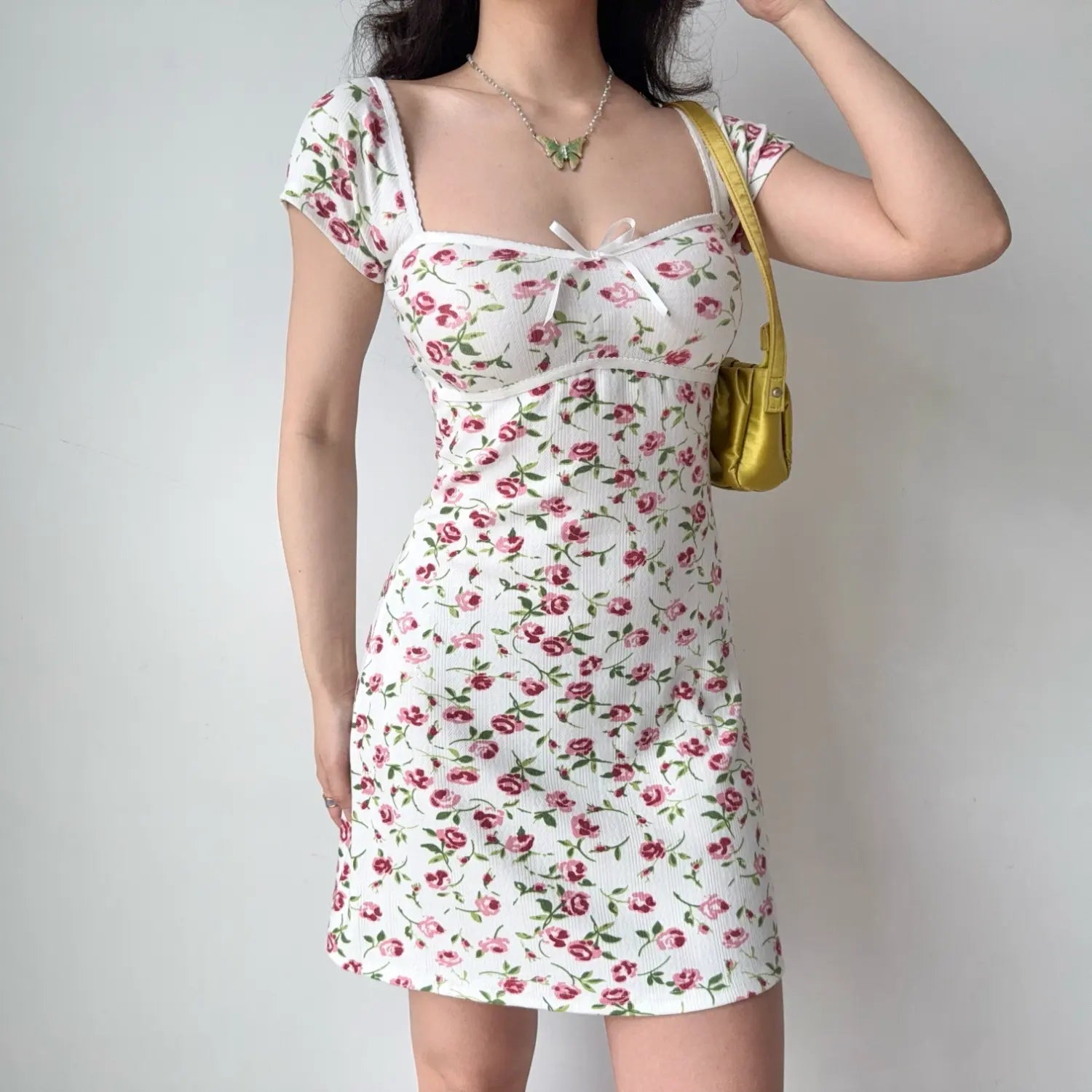 Front lifestyle shot on model of allover pink rose printed ribbed mini dress, square neck, cute front bow detail