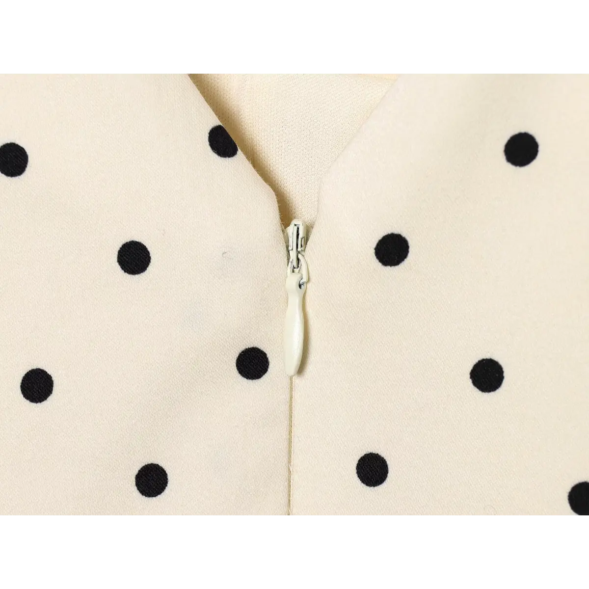 Center back invisible zipper close-up, matching cream tape zipper on V-neck polka dot mini dress inner seam.
