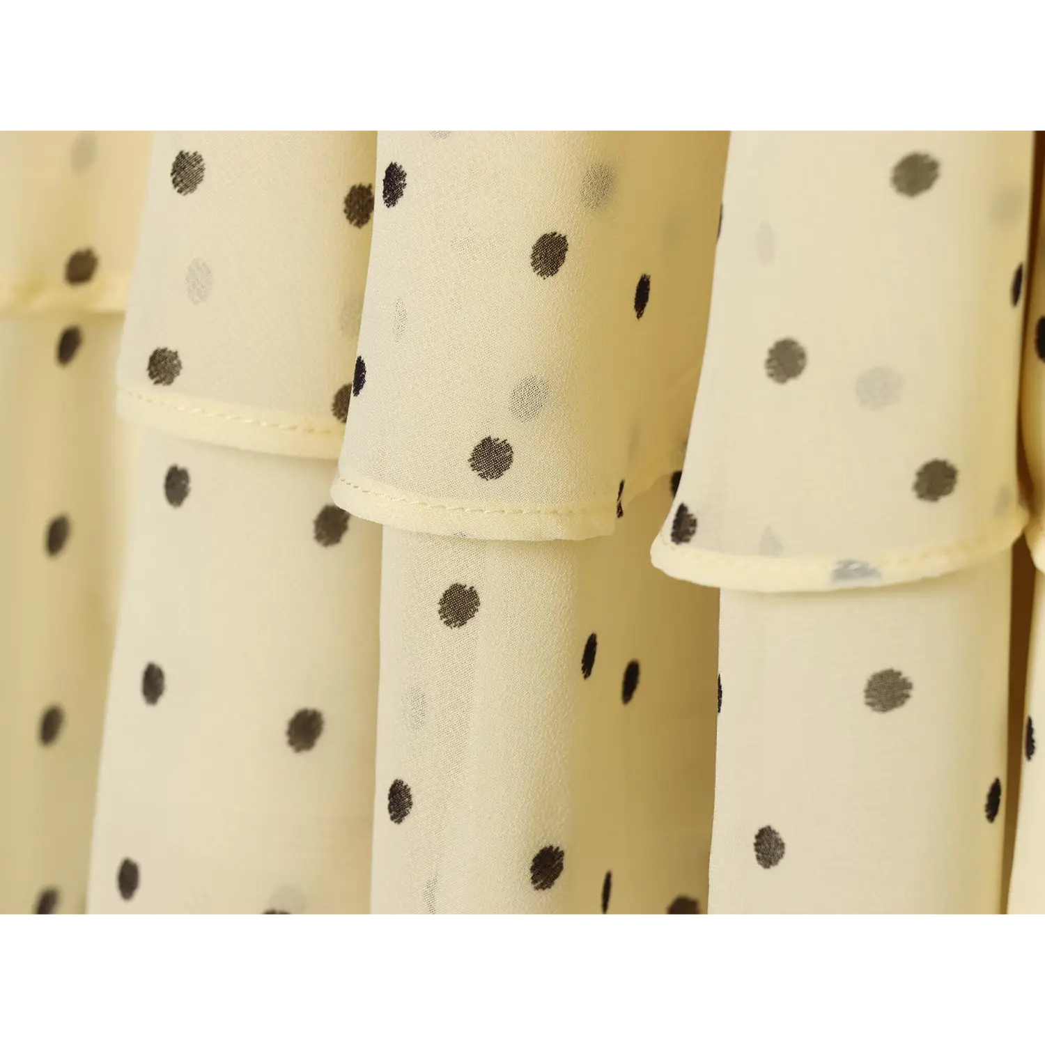 Close-up of double tiered chiffon skirt hem, showing fine overlock stitching and mixed dark gray polka dot print on sheer cream fabric