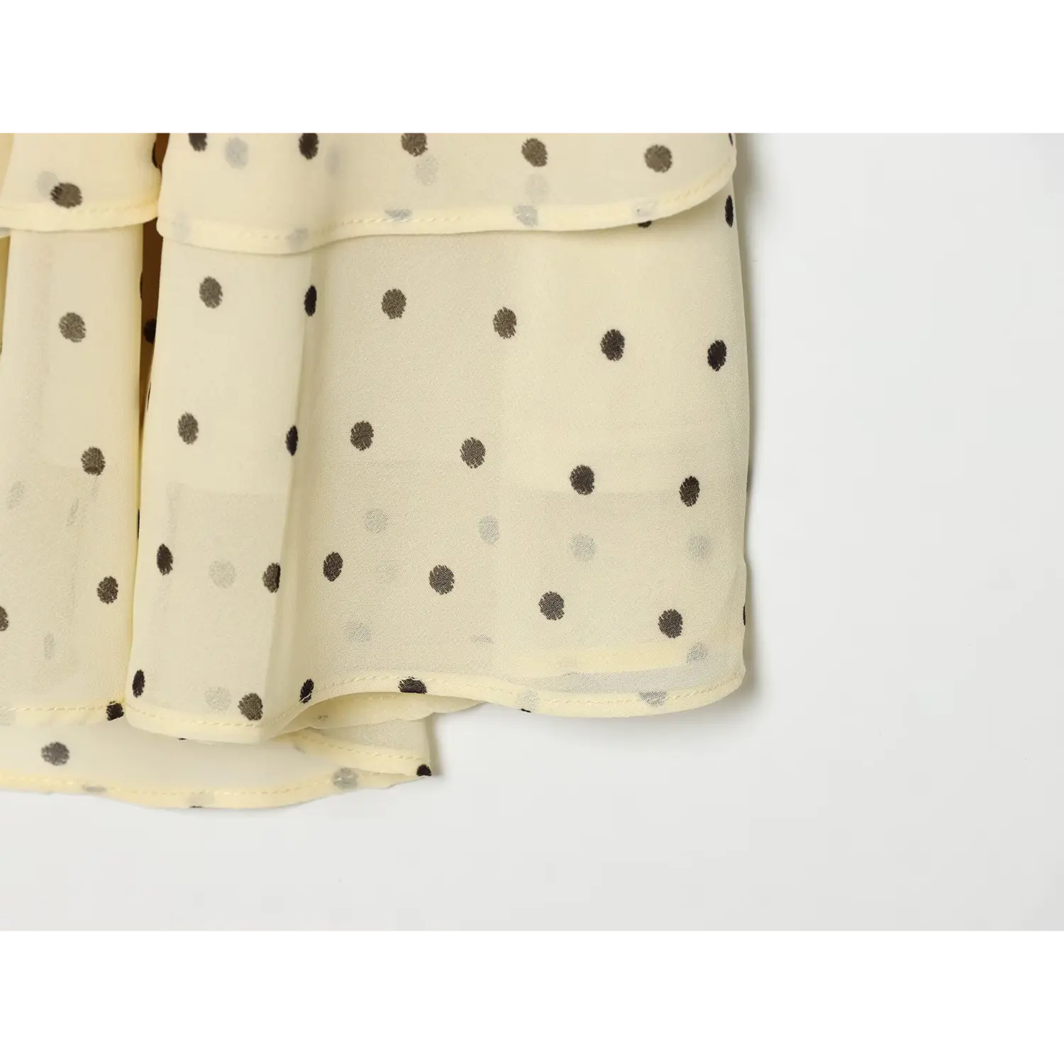 Macro shot of lightweight semi-sheer chiffon, displaying varying size gray polka dot pattern and neat hem stitching