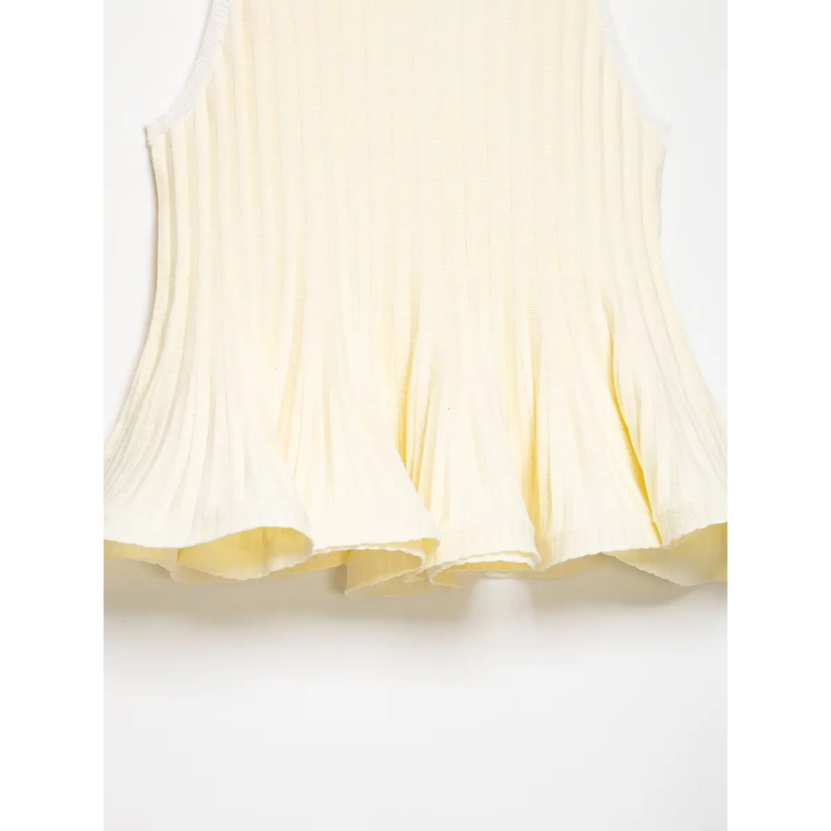  Hem view of the cream ribbed knit peplum top, showing the flared, double-layered ruffled hem and vertical ribbed texture