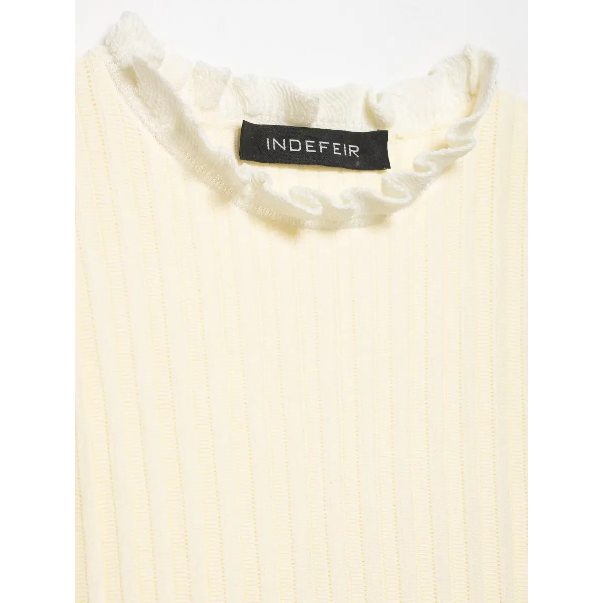 Close-up of the neckline on the cream knit top, showing the ruffled frill trim and "INDEFEIR" brand label