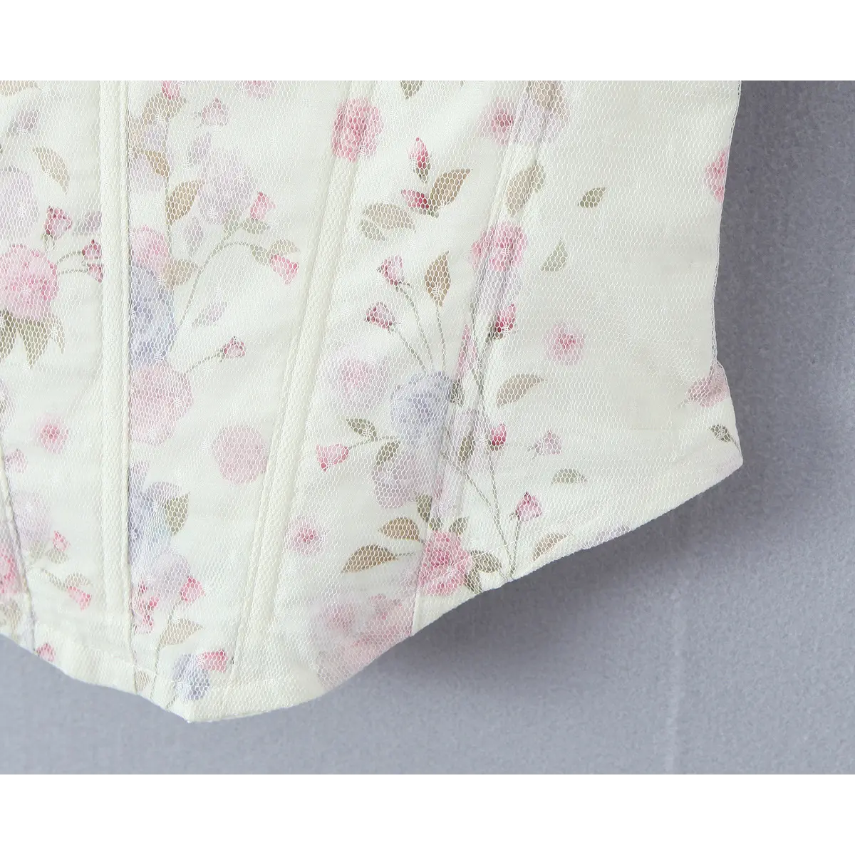 Close-up of curved corset hem with boning structure and floral mesh overlay.