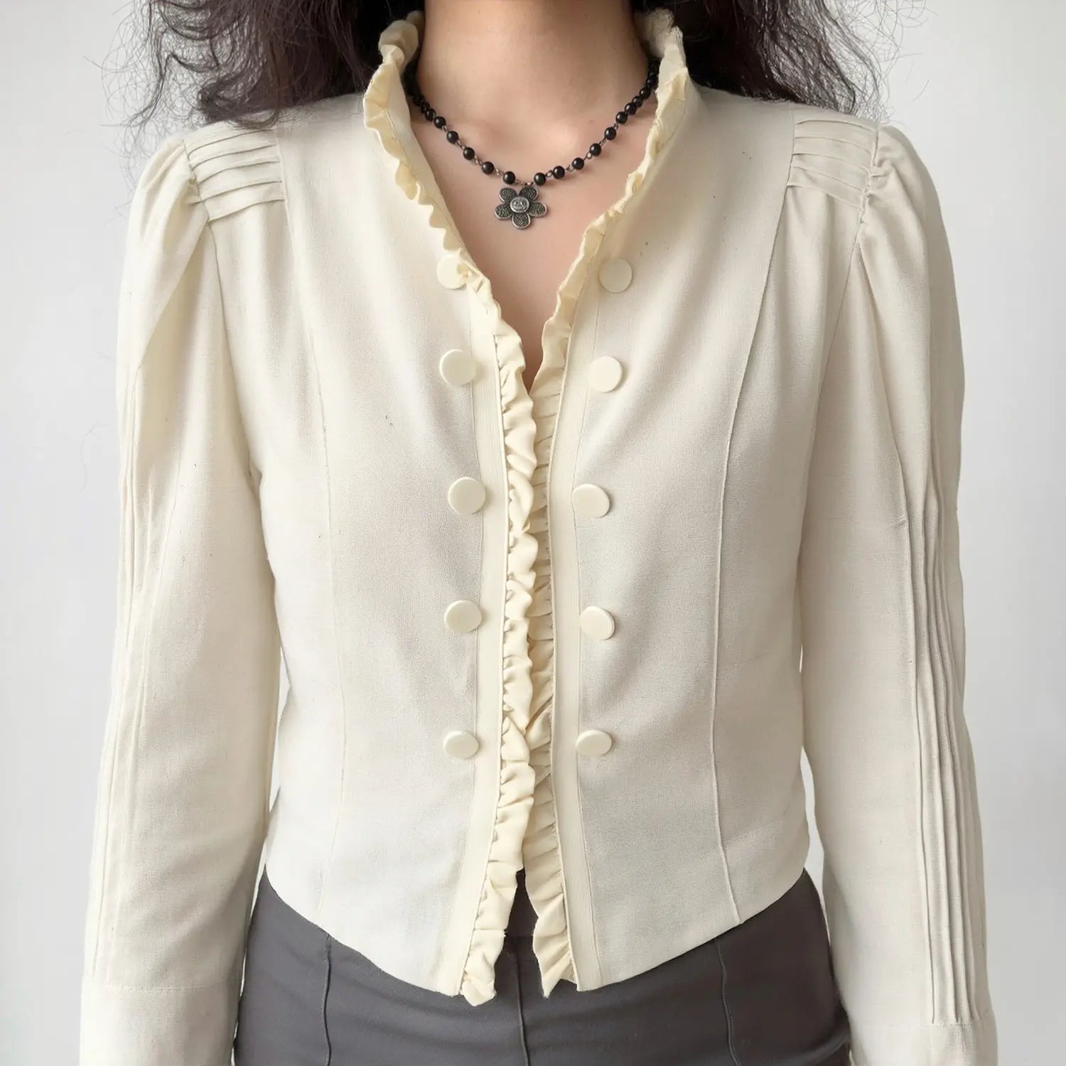 Model wearing cream ruffle stand‑collar cropped jacket, double button placket, pleated puff shoulders, torso front shot