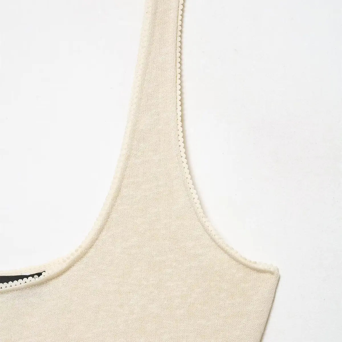 Close-up of the scoop neckline, scalloped trim, and thin straps on the cream tank dress.