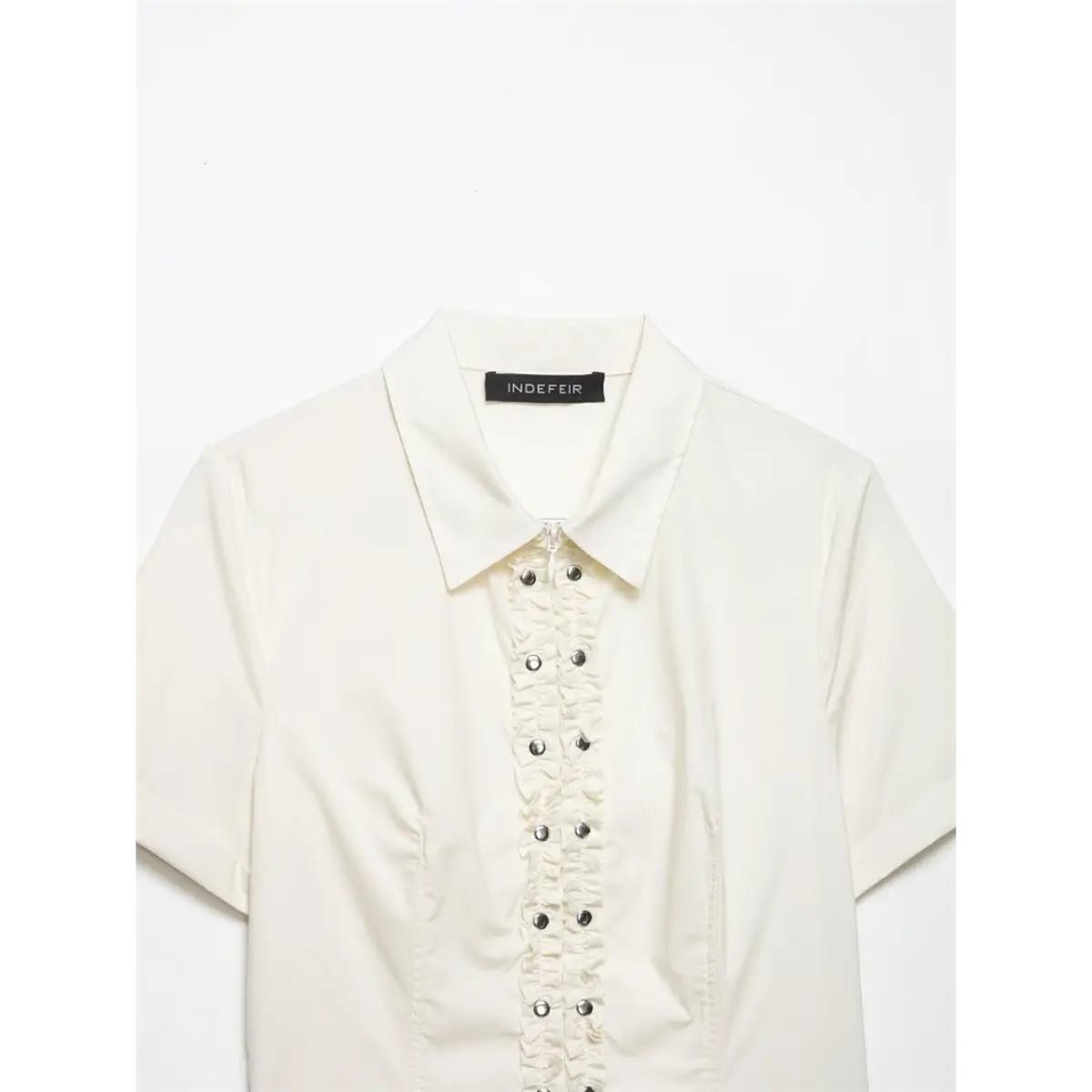 Full front shot of the cream shirt, featuring the brand label, ruffled placket, and short sleeves
