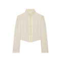 Cream ruffle stand‑collar cropped jacket front view, double row buttons, puff pleated shoulders, long sleeves, pointed hem, white background