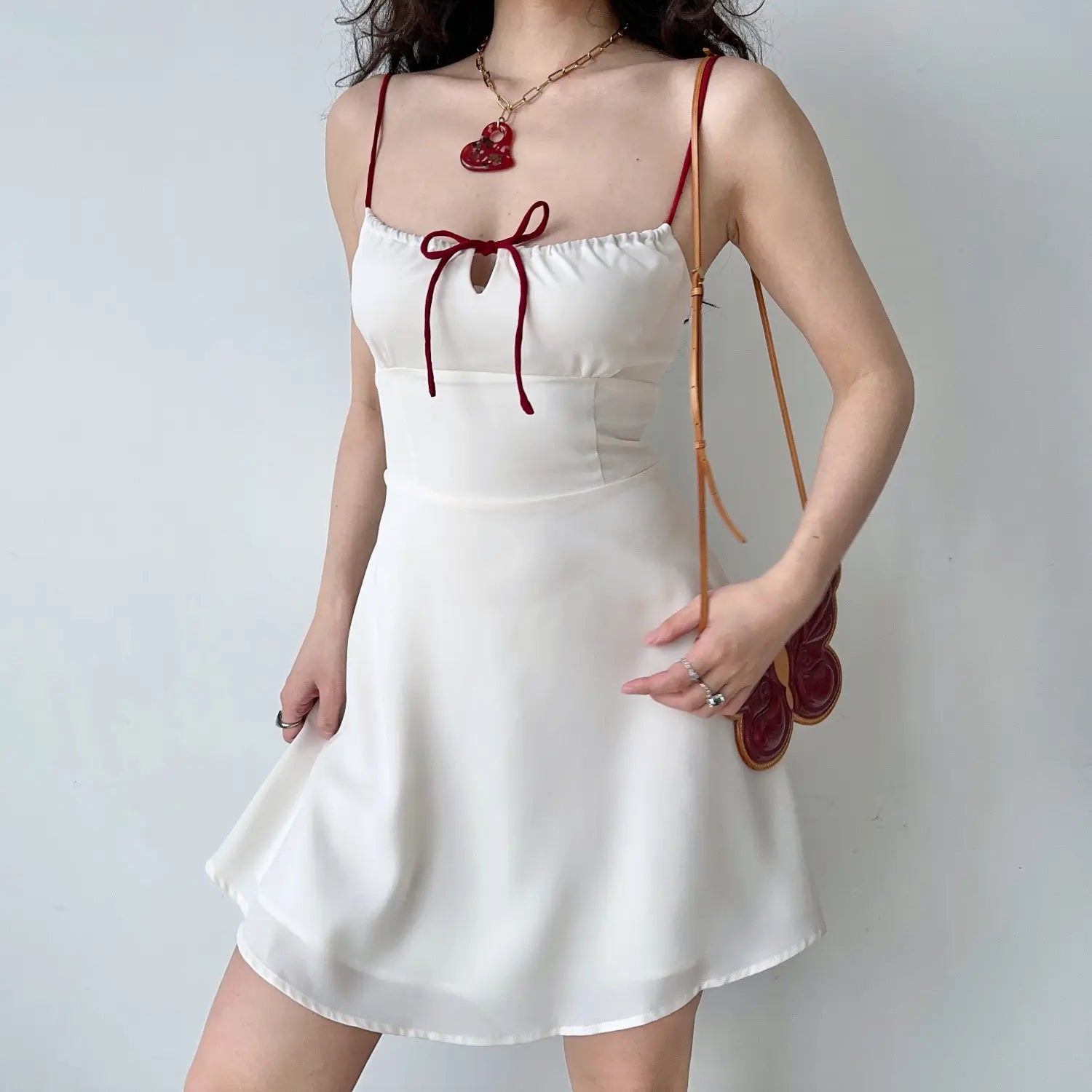 Full body studio photo cream silky cami mini dress, contrast red thin straps, front keyhole satin bow, A-line lightweight flared skirt