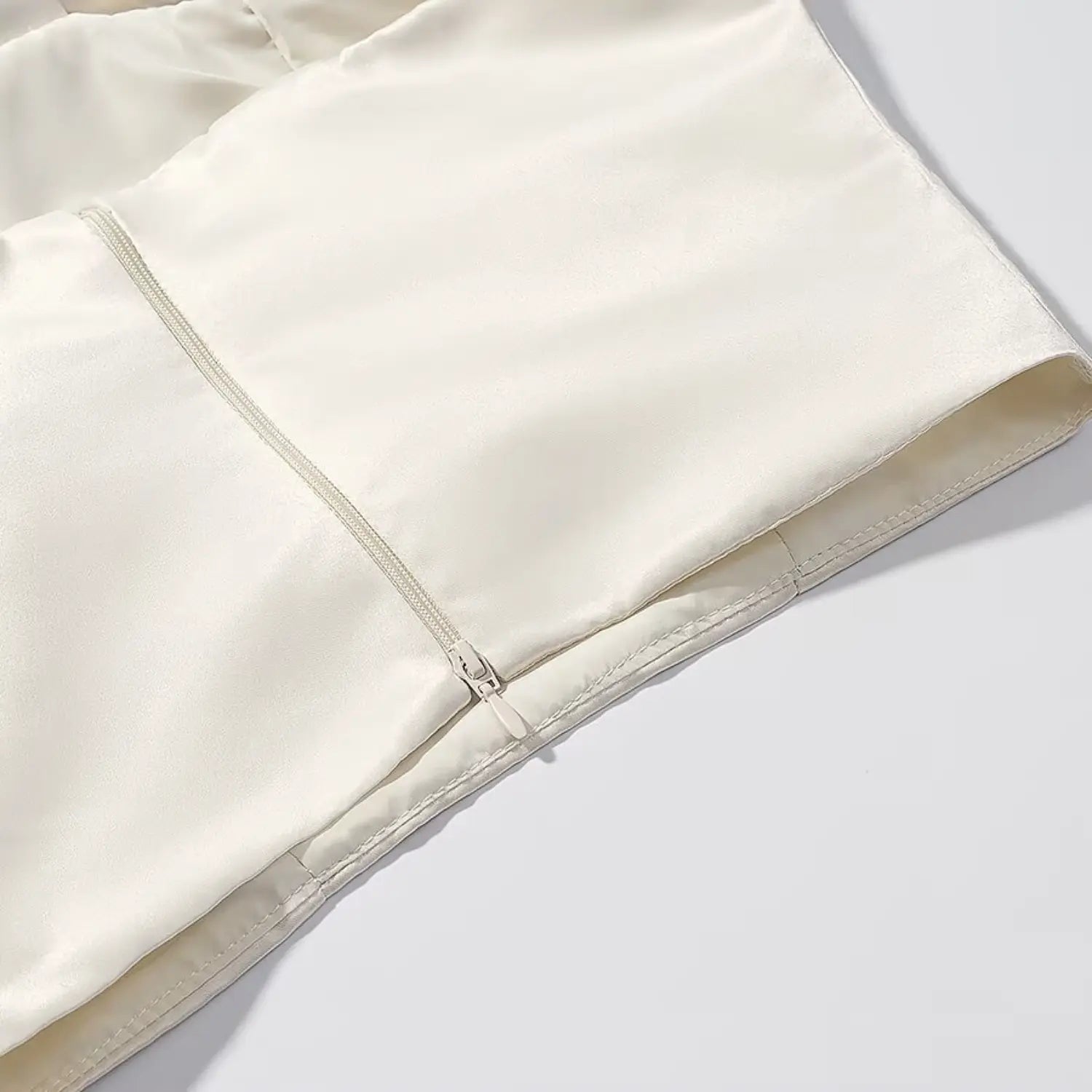 Bottom invisible zipper and hem stitching detail of cream satin crop top