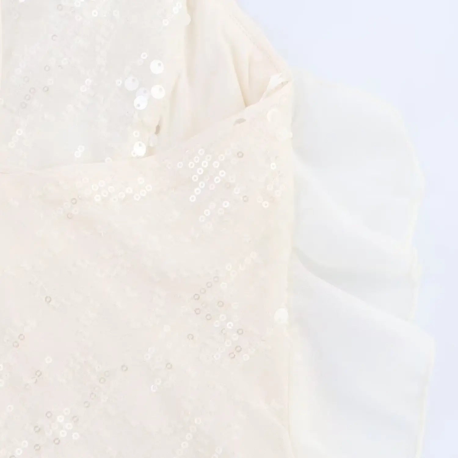Close-up of the sheer chiffon ruffle detail on the side of the cream sequined slip dress