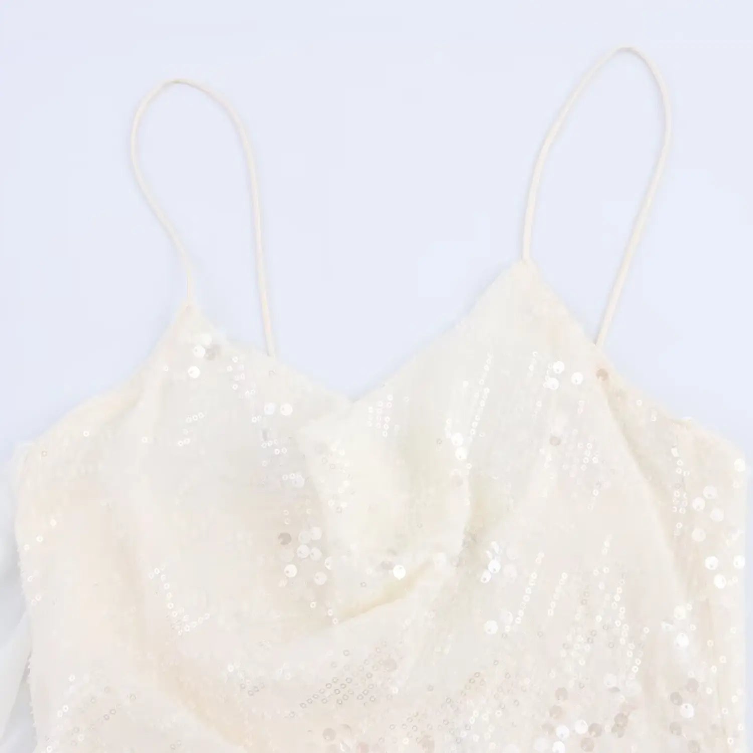 Close-up of the cowl neckline, thin straps, and scattered sequins on the cream slip dress