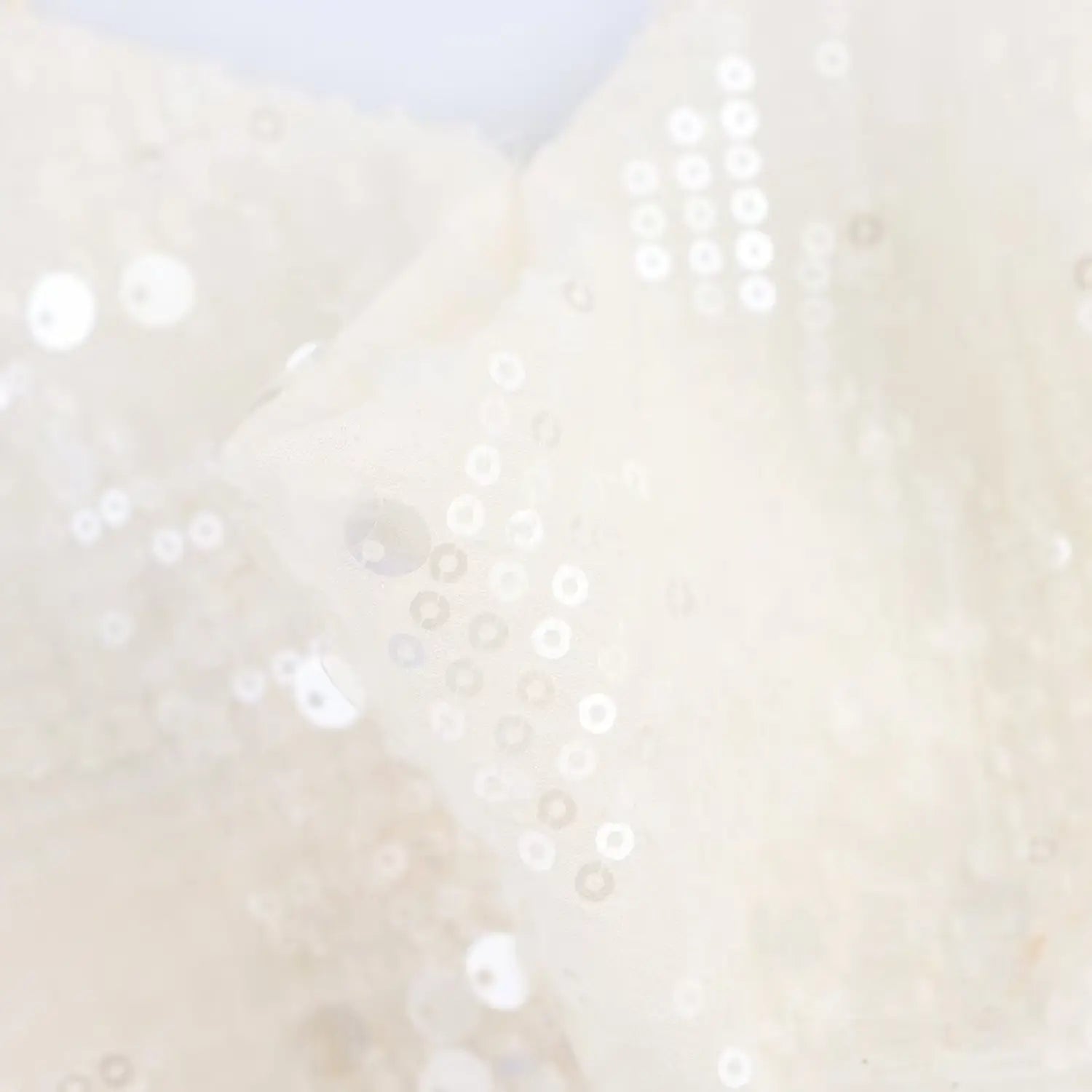 Close-up of the scattered sequins on the mesh fabric of the cream slip dress, showing the sheen and pattern