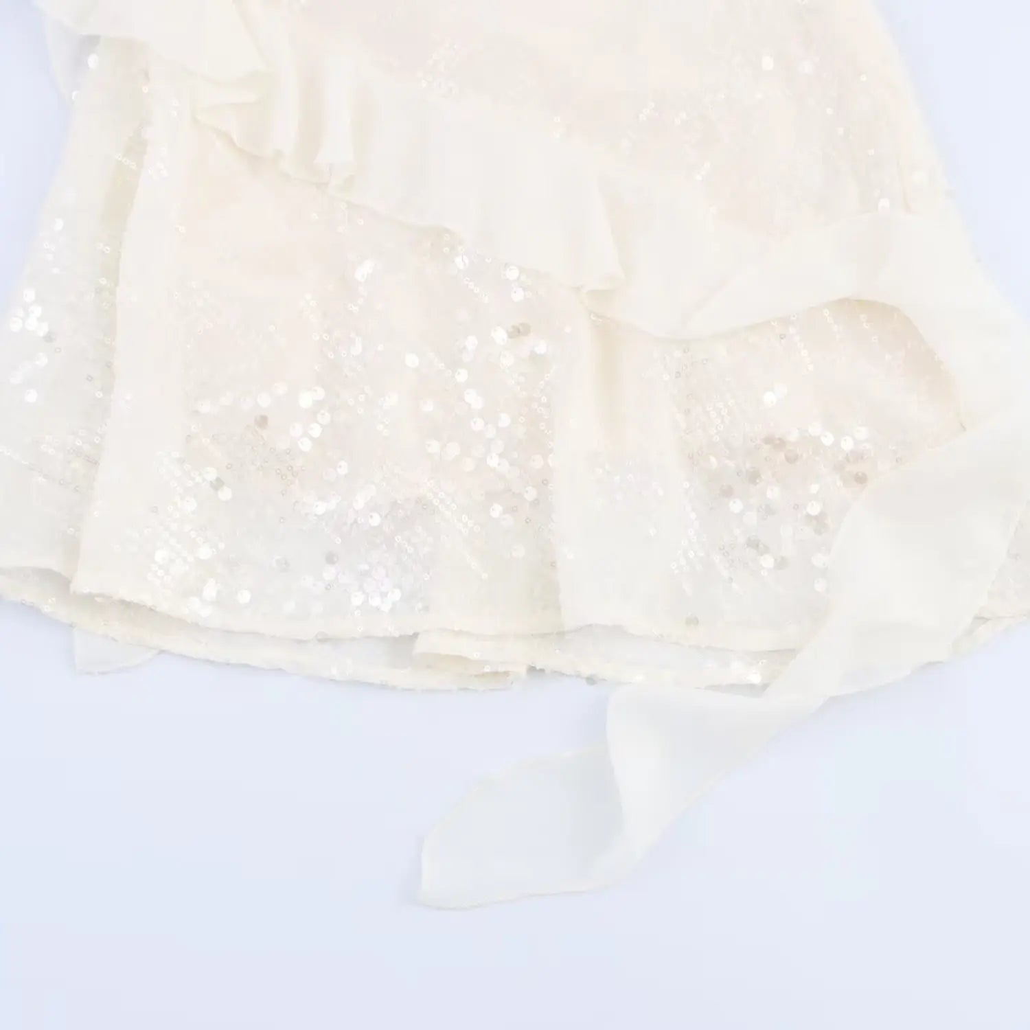 Close-up of the flared chiffon ruffle hem and hanging ribbon detail on the cream sequined dress