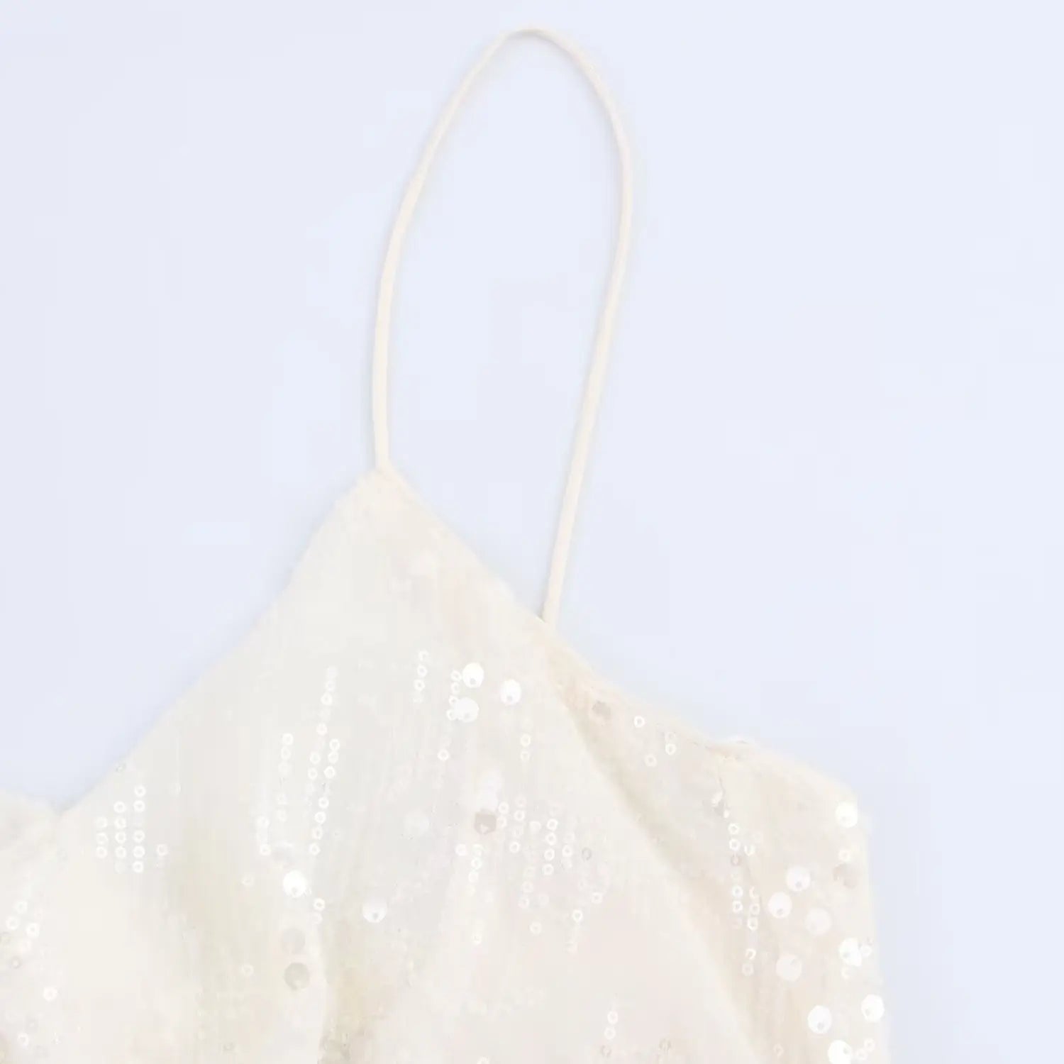 Angled close-up of the thin strap and cowl neckline on the cream sequined mini dress