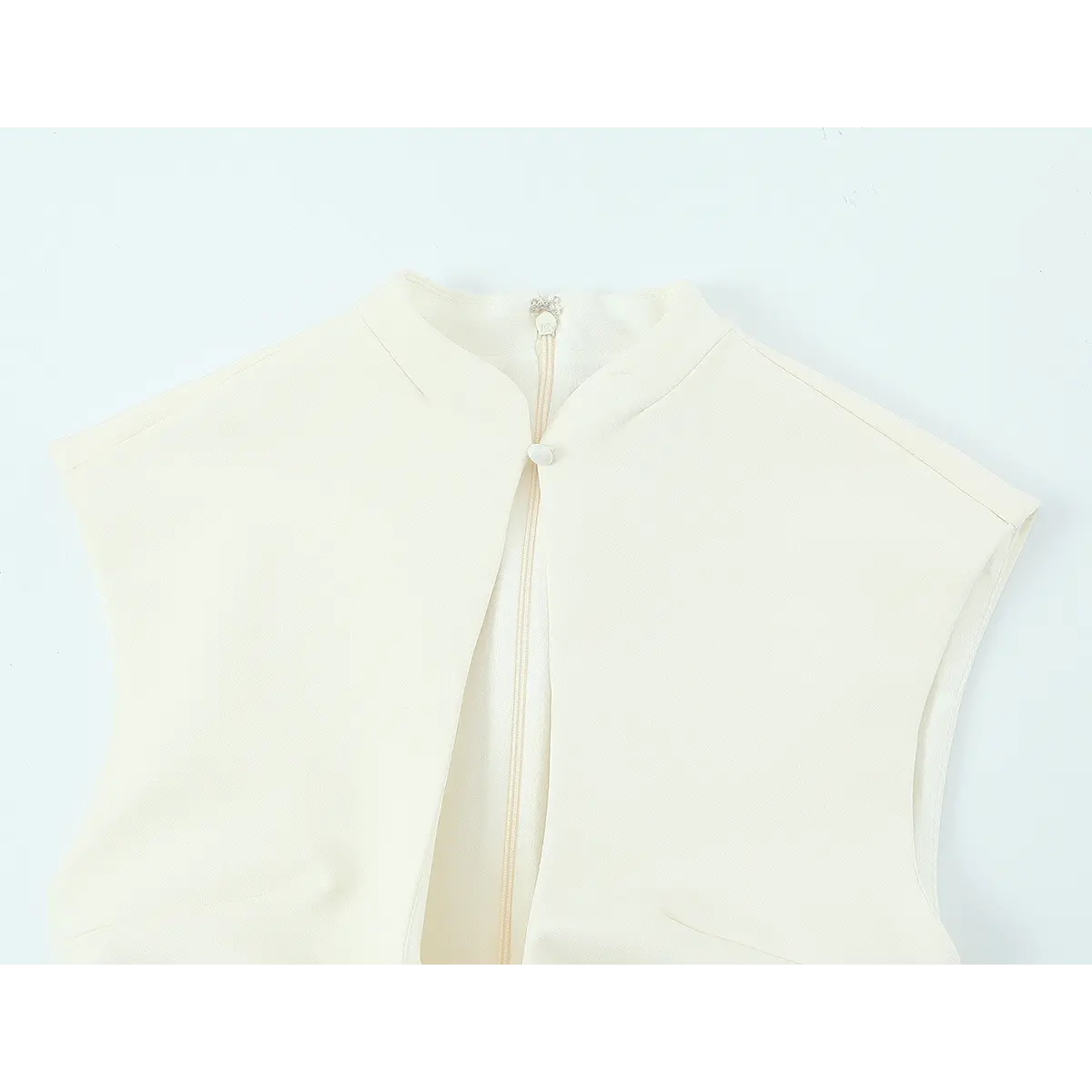Neckline detail of cream sleeveless dress, showing the mandarin collar, keyhole button, and back zipper