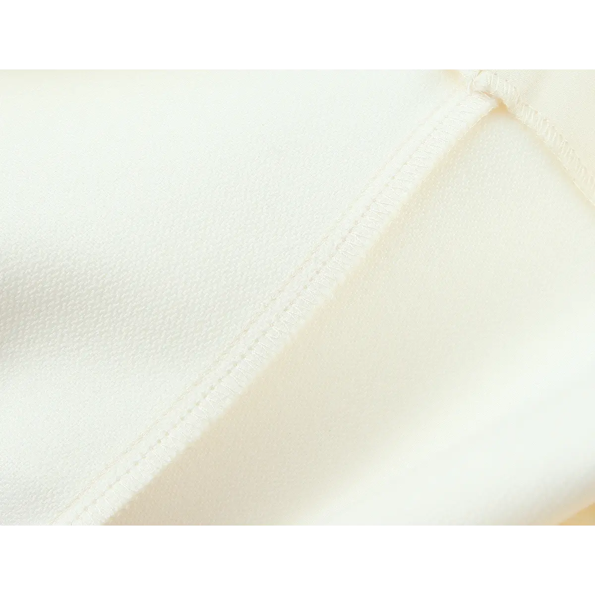 Close-up of the seam stitching on the cream sleeveless dress, showing the fabric texture and construction
