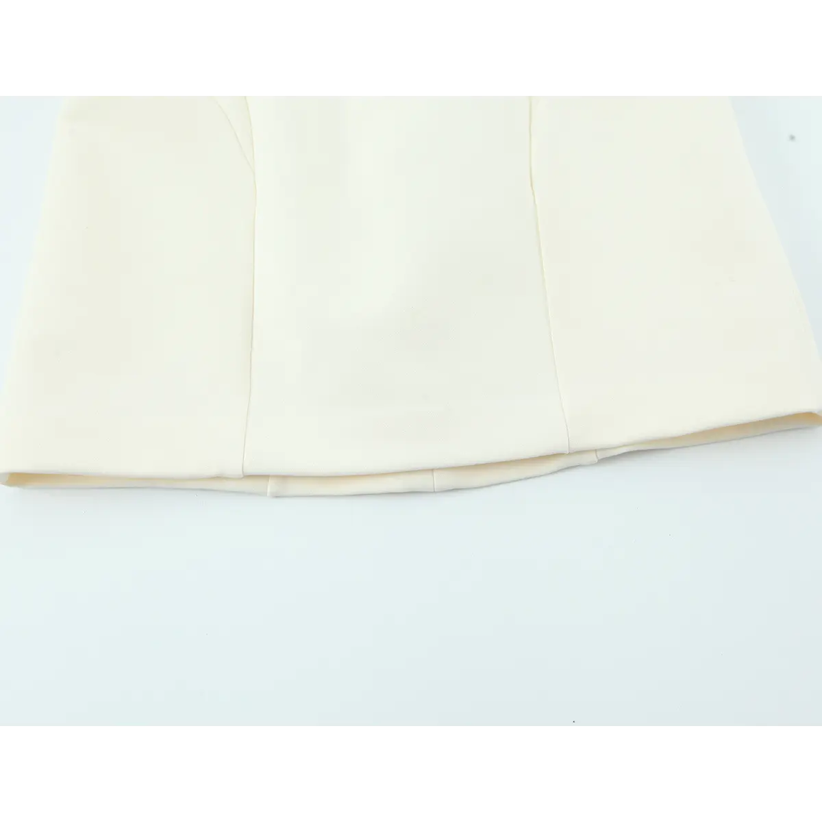 Bottom hem view of cream sleeveless dress, showing the structured panel seams and clean finish