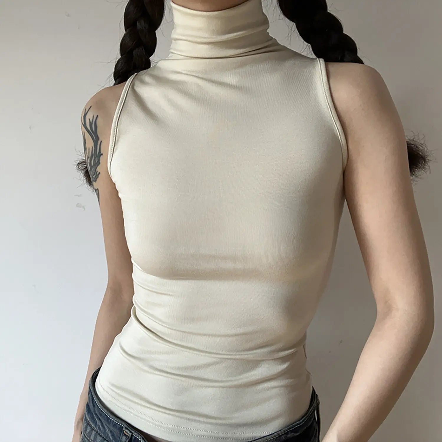 Front torso shot of model wearing cream sleeveless turtleneck tank top, slim fit ribbed knit fabric