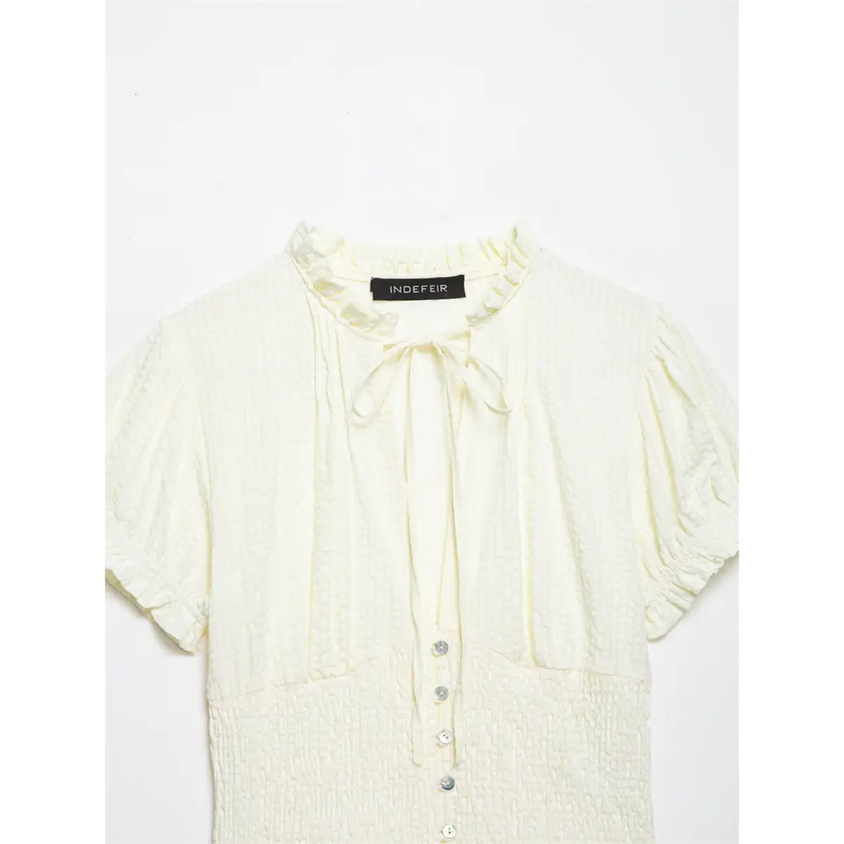 Neckline detail of cream blouse, showing the ruffled collar, tie closure, and brand label