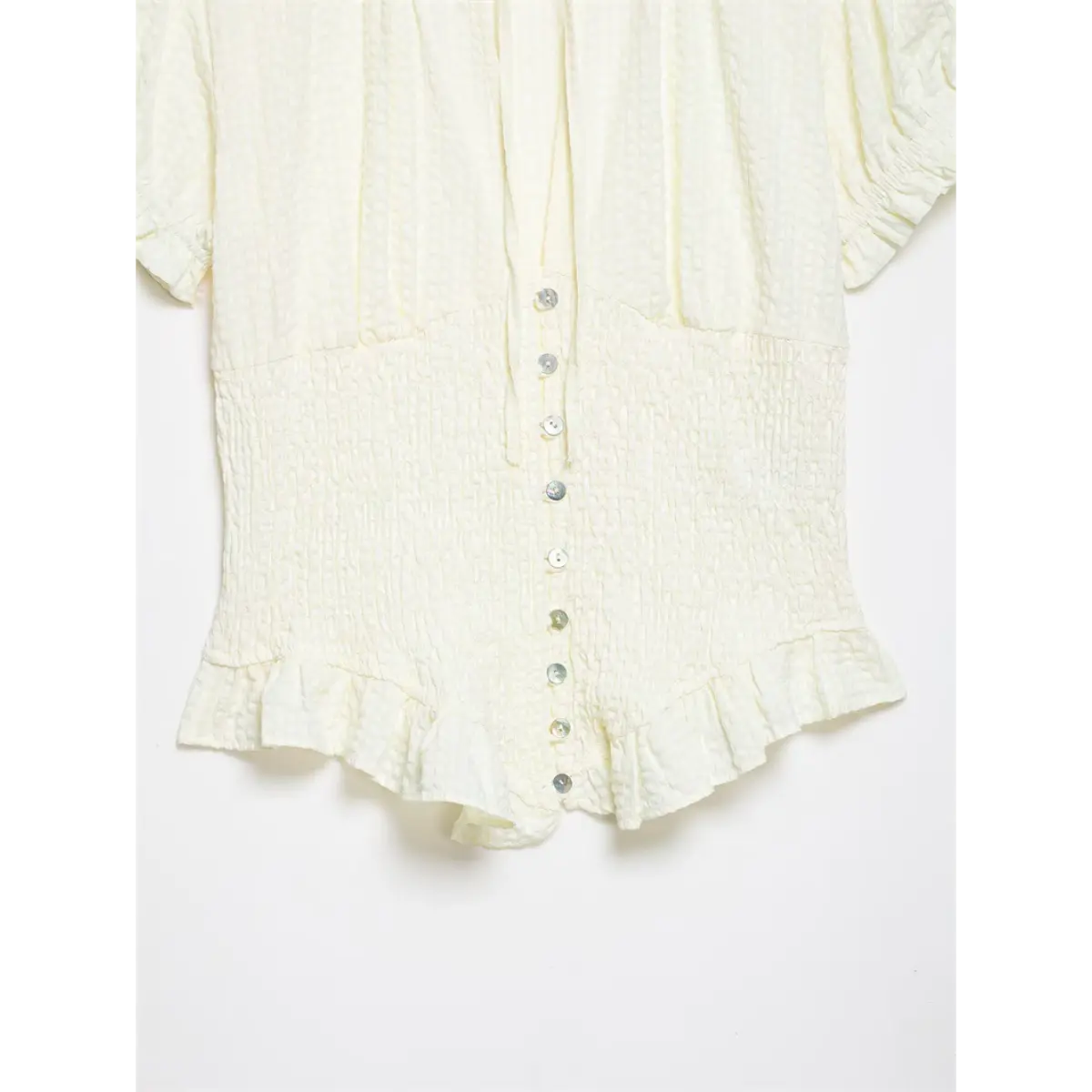 Full front shot of cream textured blouse, with shell buttons down the placket and ruffled hem