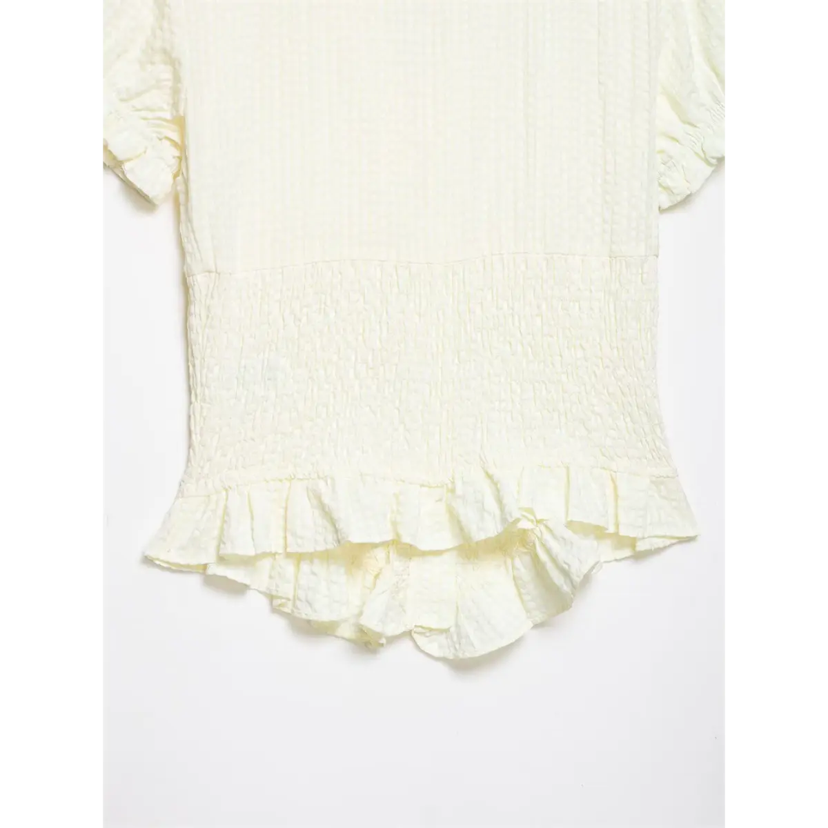 Bottom hem detail of cream textured blouse, showing the layered ruffled finish