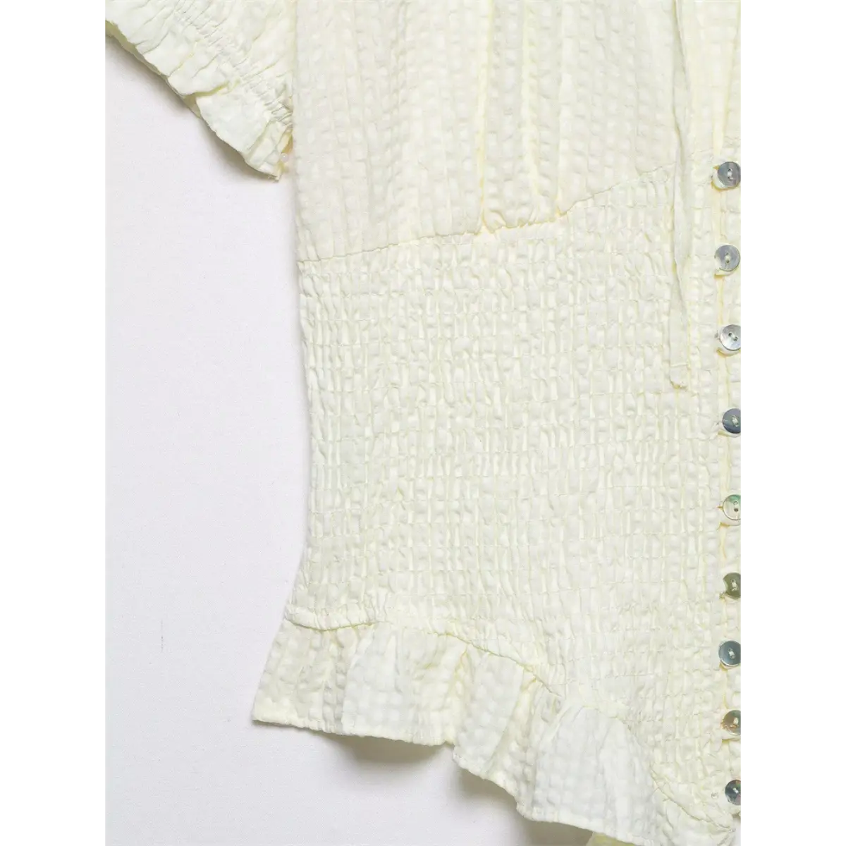 Side view of cream textured blouse, showing the smocked waist, shell buttons, and ruffled hem