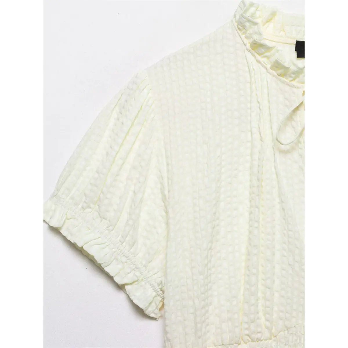 Sleeve and shoulder detail of cream blouse, showing the textured fabric and gathered puff sleeve