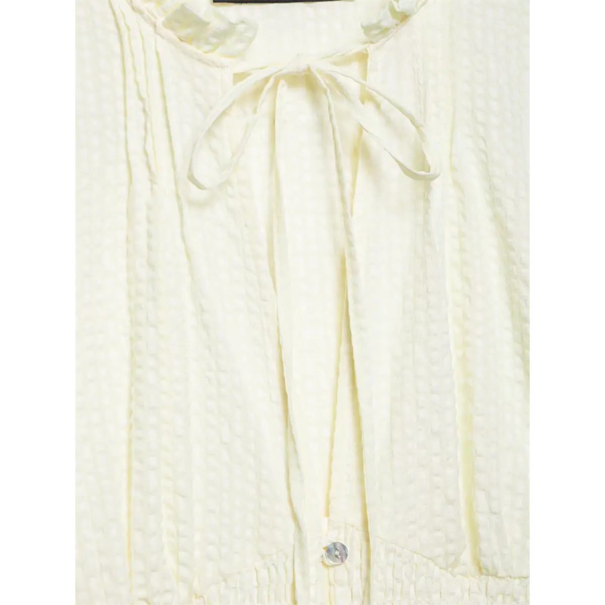 Close-up of the tie closure at the ruffled collar of the cream textured blouse