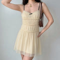 Model wearing a cream smocked cami mini dress, showcasing the tiered bodice, flowy skirt, and delicate contrast details.