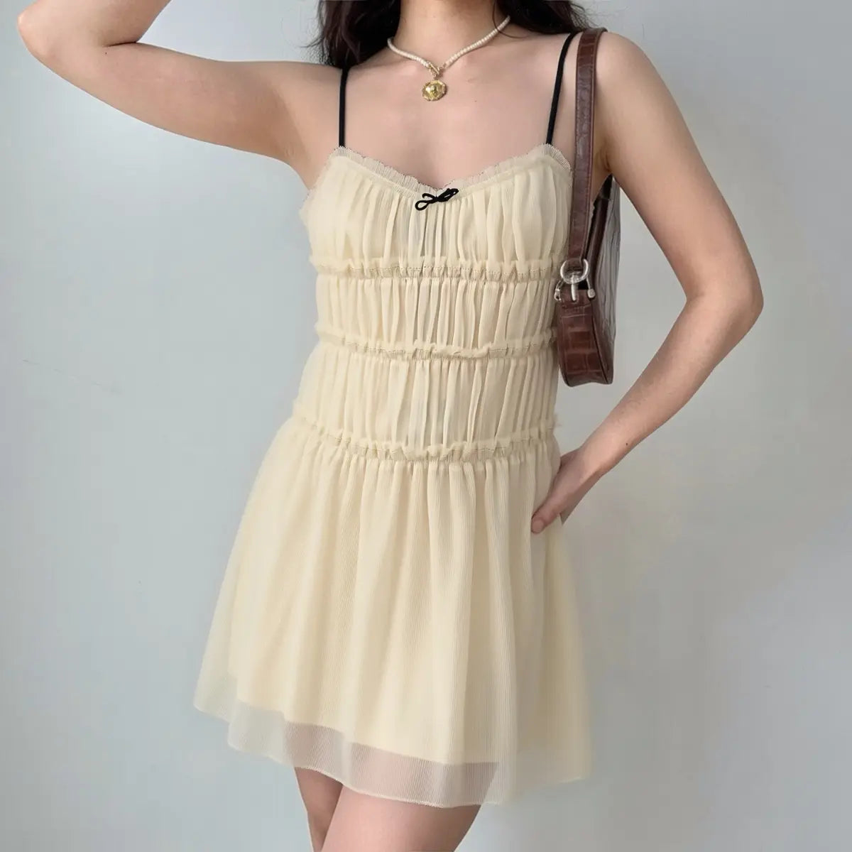 Model wearing a cream smocked cami mini dress, showcasing the tiered bodice, flowy skirt, and delicate contrast details.
