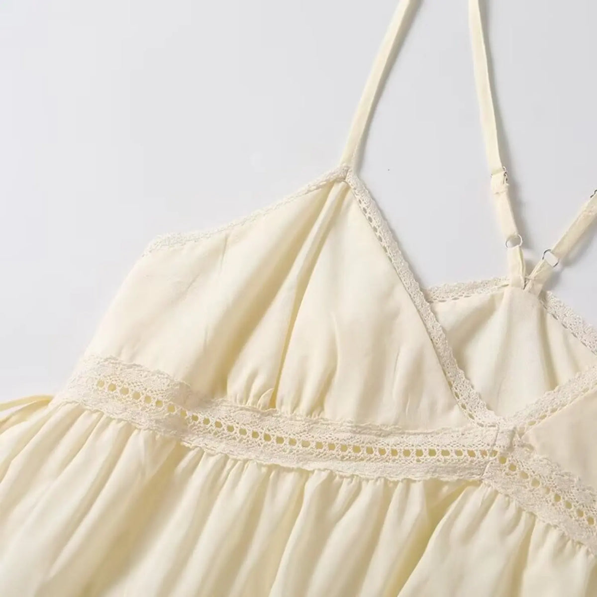 Closeup of cream cami top v neck and lace trim, adjustable cross back straps and soft fabric
