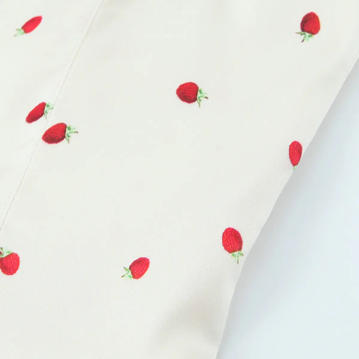 Close-up of the fabric on the cream cami top, showing the smooth texture and scattered strawberry print