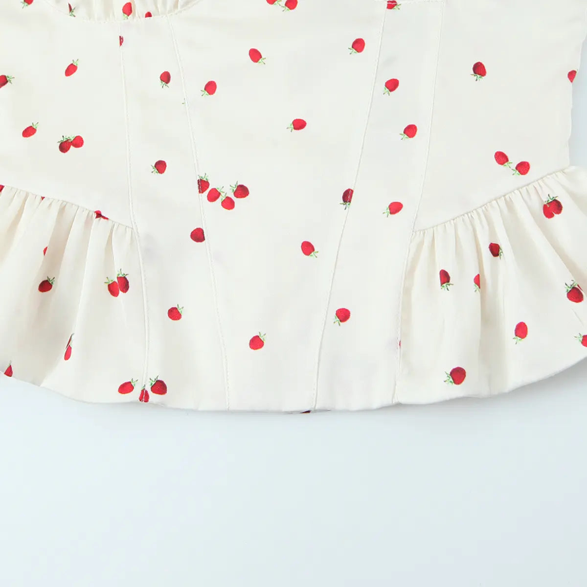Hem view of the cream strawberry print cami top, showing the peplum ruffle and gathered waist seam