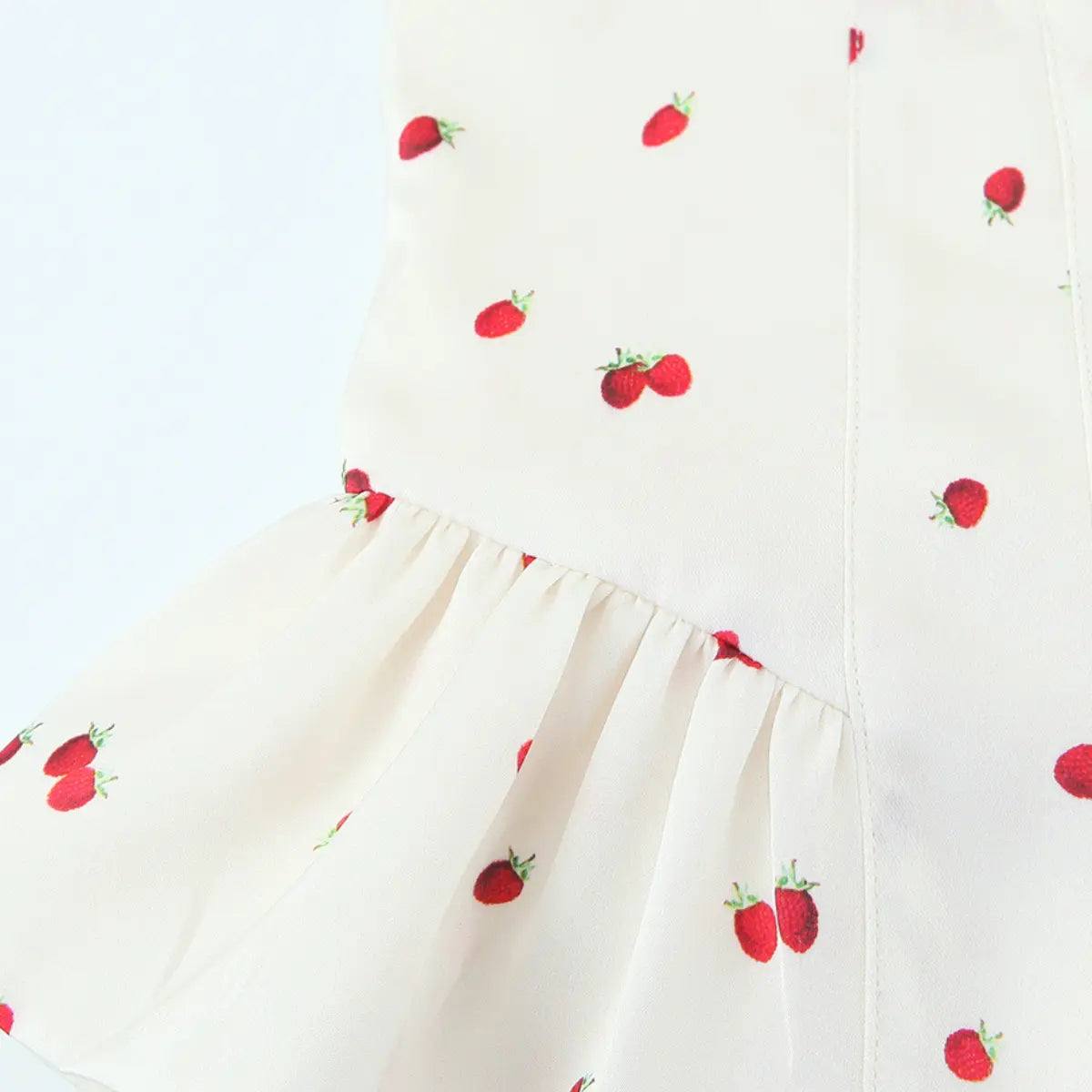 Close-up of the peplum ruffle on the cream cami top, showing the gathered seam and strawberry print