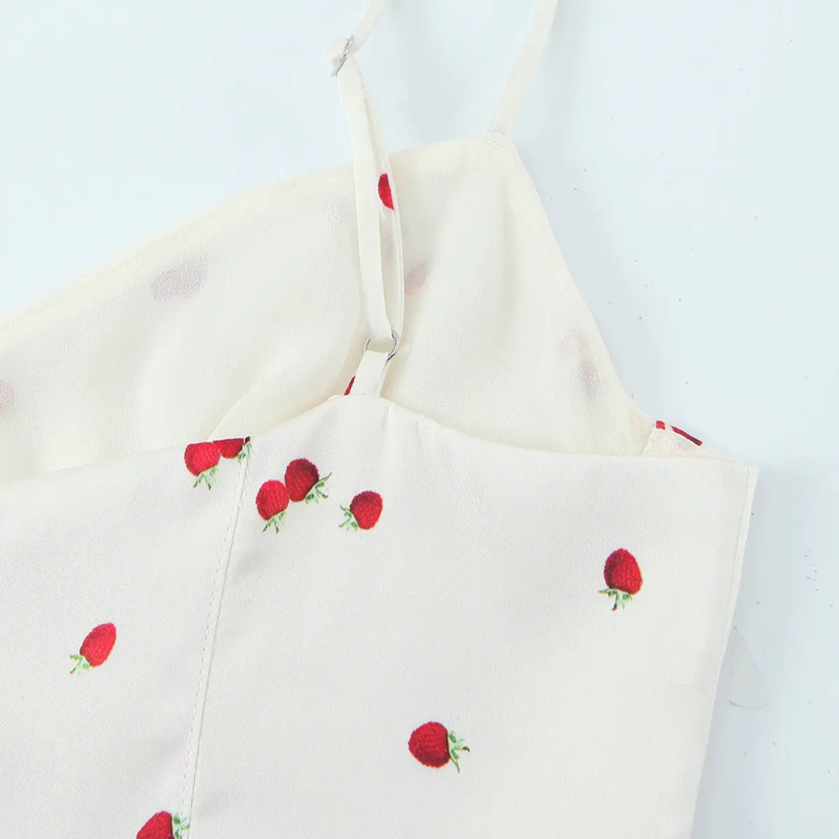 Close-up of the adjustable strap on the cream cami top, showing the slider and smooth fabric with strawberry print