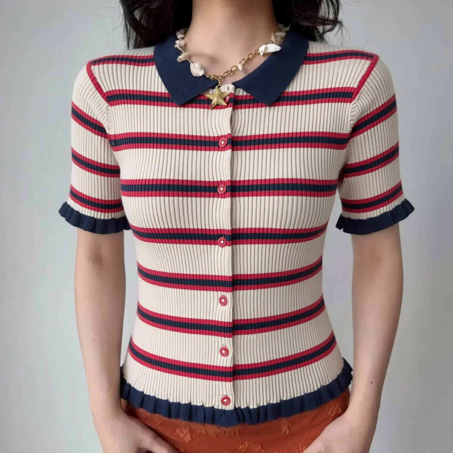 Front lifestyle shot on model, navy polo collar striped knit cardigan, full front button design, ruffled sleeve and hem, matched with shell starfish necklace and orange bottoms, casual retro summer outfit
