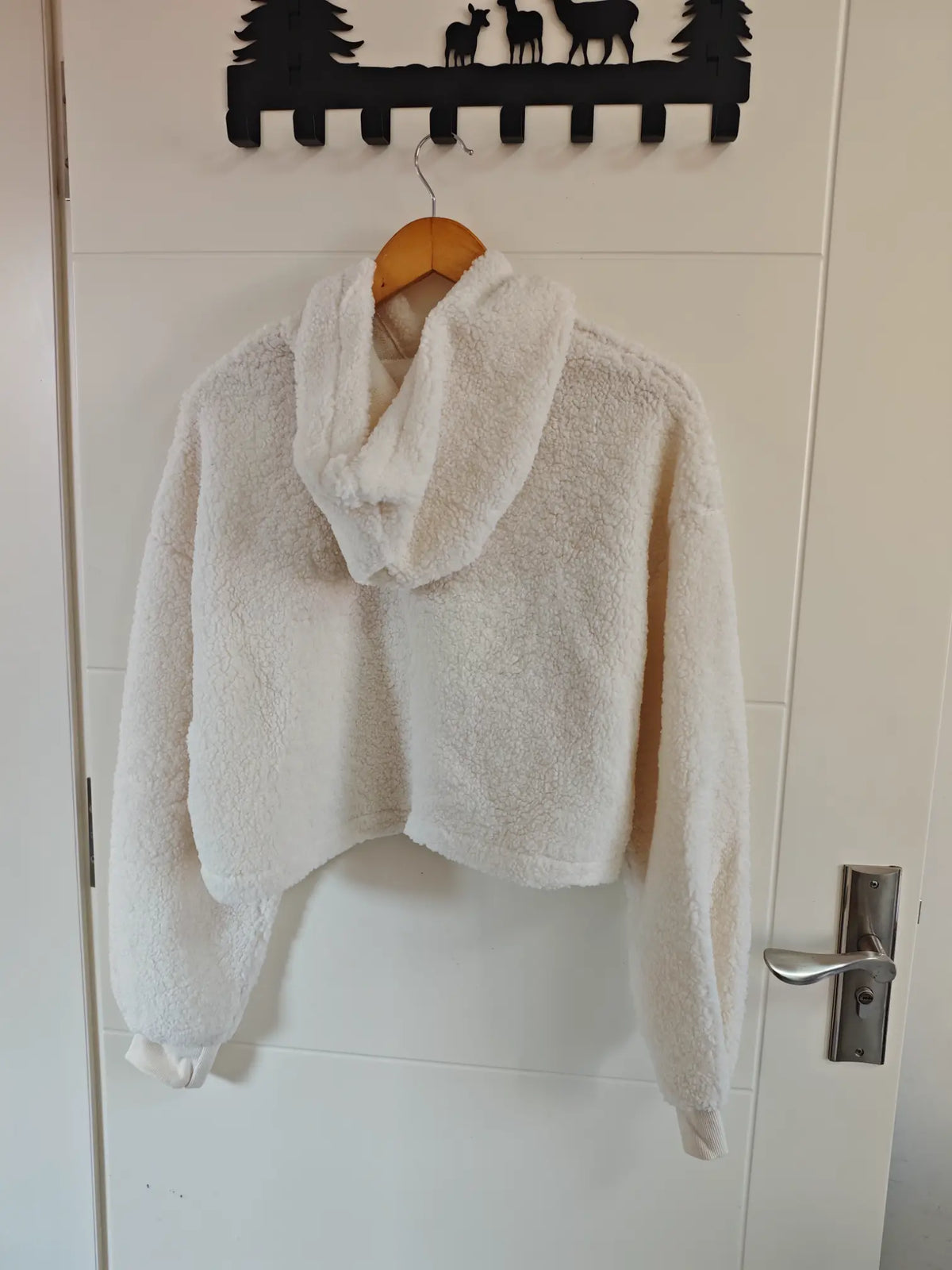 Cream teddy fleece hooded cropped sweatshirt hanging on door, back view