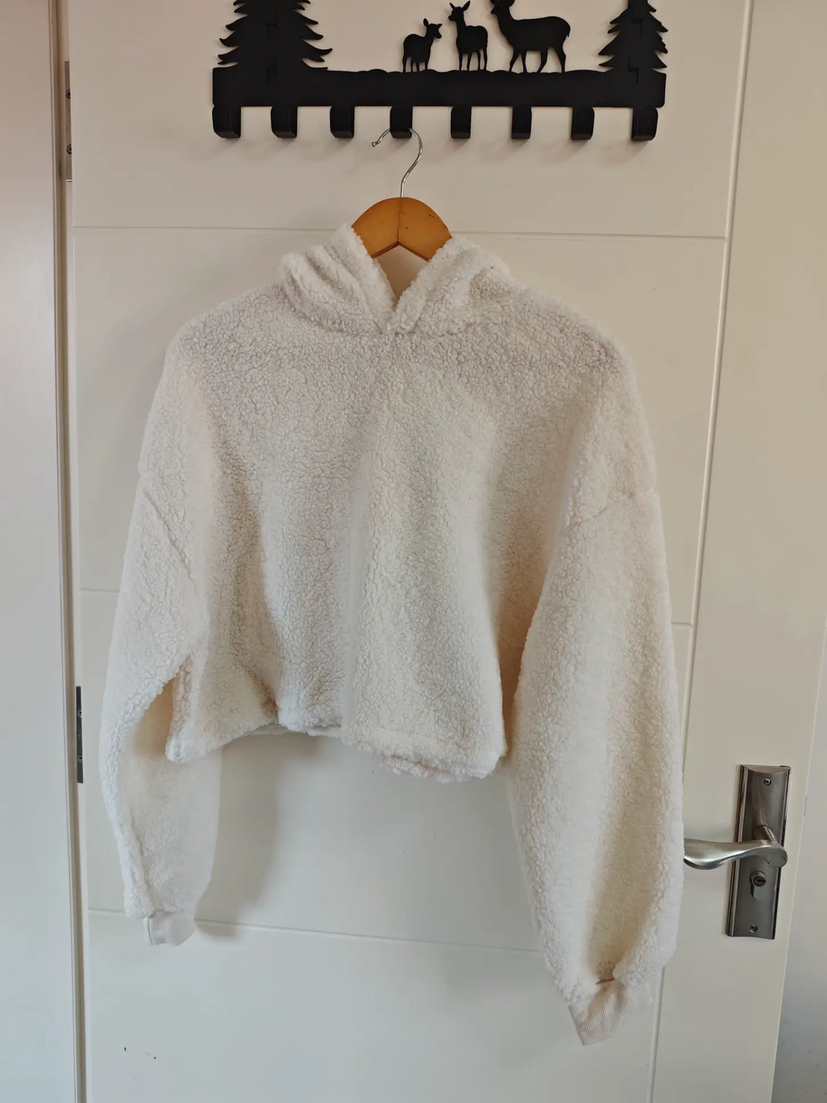 Cream teddy fleece hooded cropped sweatshirt hanging on door, front view
