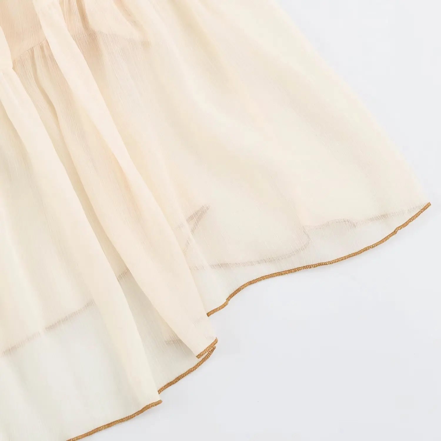Close-up skirt hem with brown piping trim on cream sleeveless tiered maxi dress
