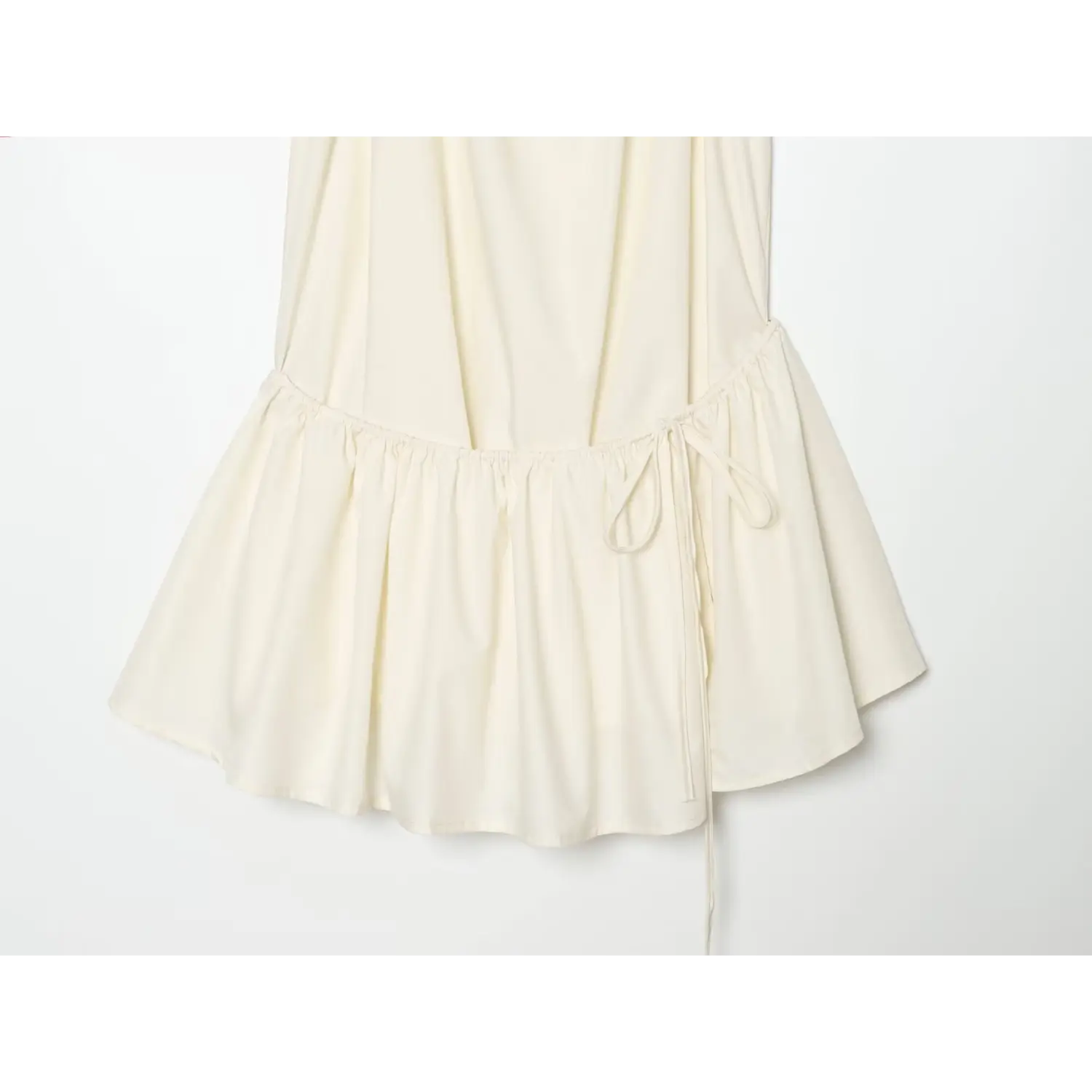 Close‑up of elastic gathered waist with side drawstring tie, tiered ruffle skirt hem on cream halter mini dress