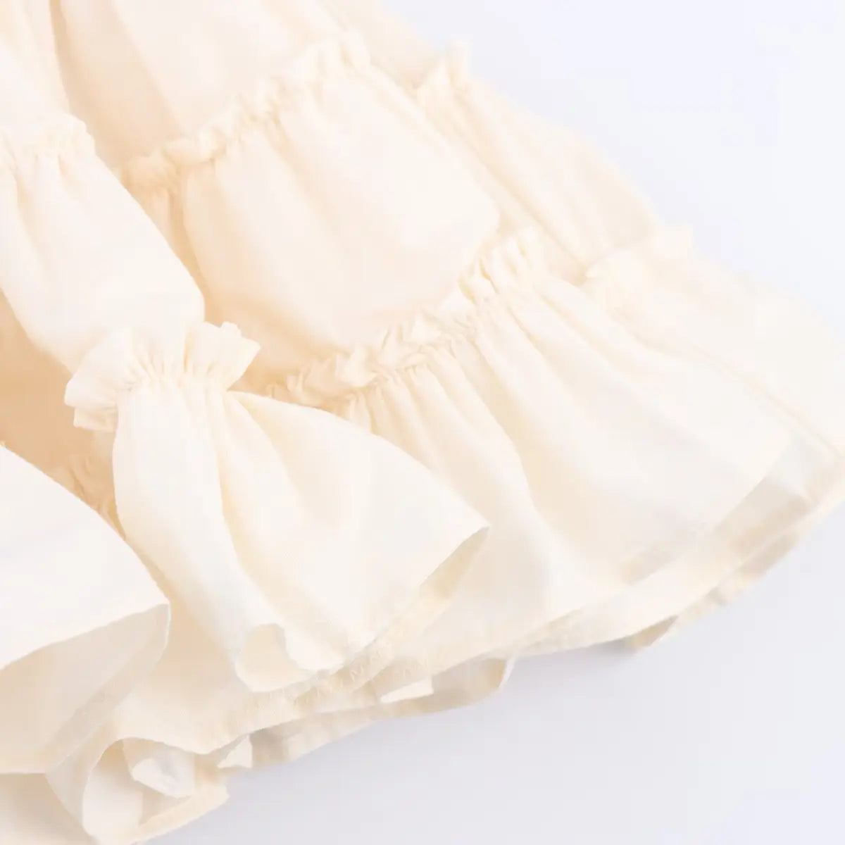 Close-up of the tiered ruffled skirt hem on the cream ribbed knit dress