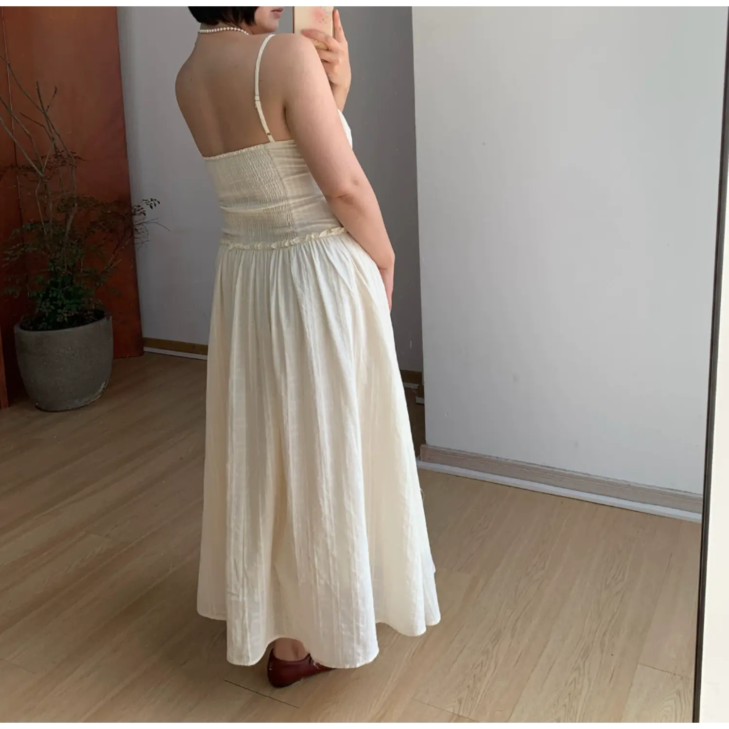 Back side indoor mirror shot of textured empire waist maxi slip dress, full elastic smocked back bodice for stretch fit, thin single adjustable spaghetti strap, full gathered flowy A-line skirt, subtle vertical waffle fabric drape display, burgundy flat shoes