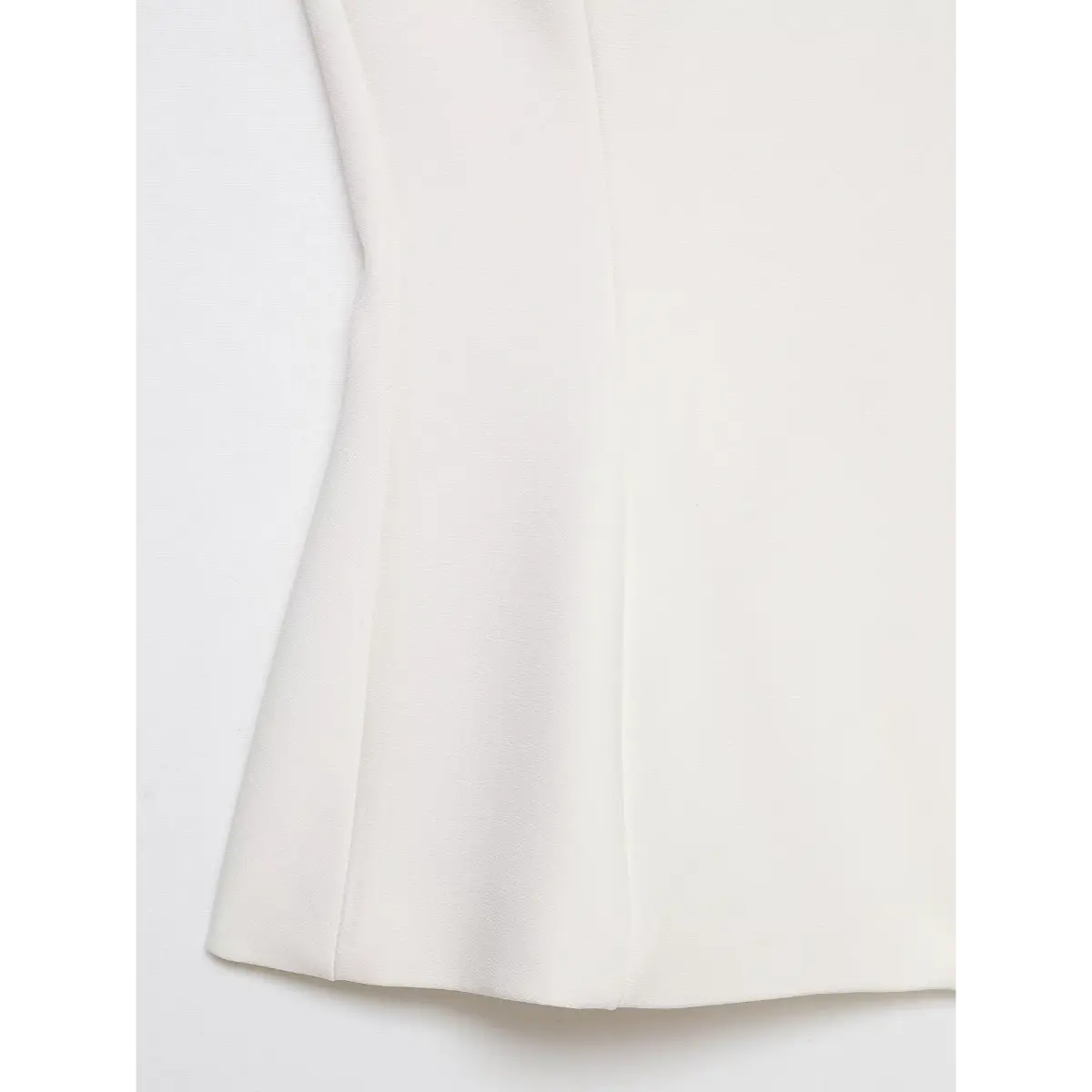  Close-up of the peplum hem and fabric texture on a cream-white halter top.