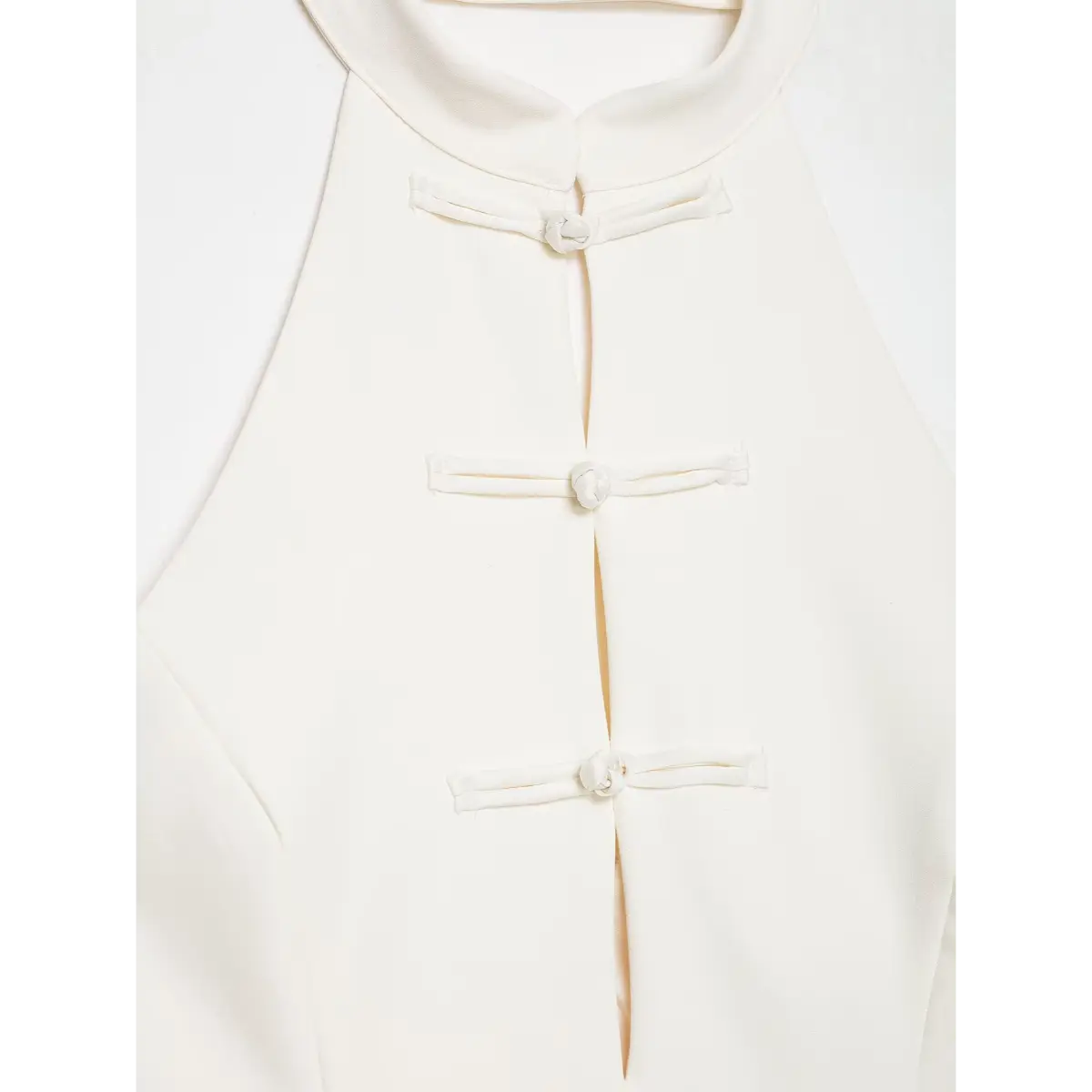 Close-up of the neckline and traditional Chinese knot buttons on a cream-white halter top.