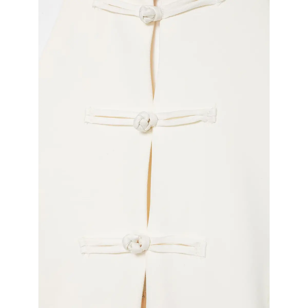 Close-up of traditional Chinese knot buttons on a cream-white halter top.