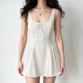 Front lifestyle shot on model of cream sleeveless mini sundress, wide straps, square neck, front corset lace-up, high waist gathered flare skirt