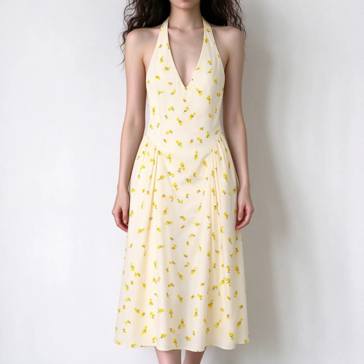 Model wearing cream halter maxi dress, deep v neck, scattered small yellow floral print, pleated flowy maxi skirt, solid white background