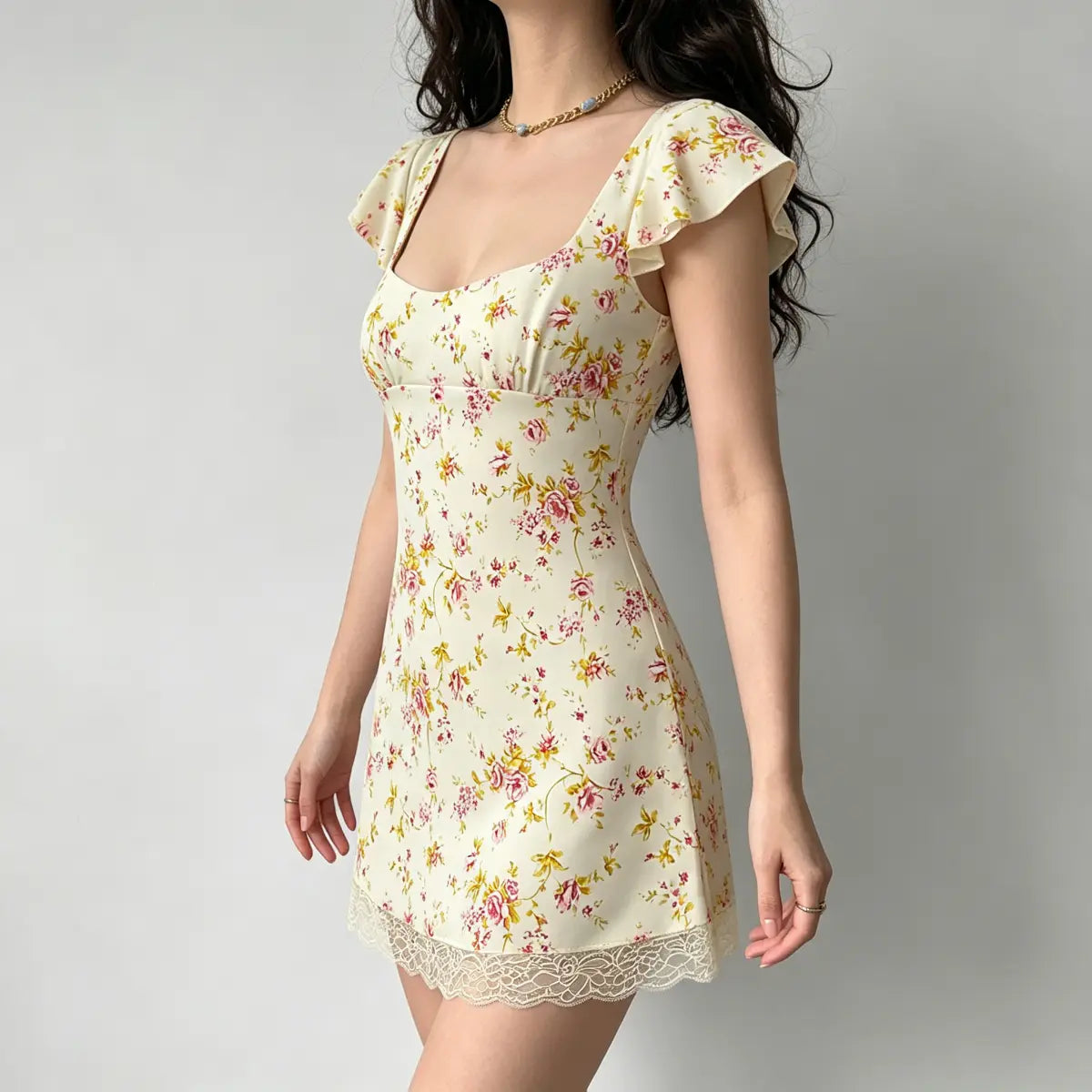 Profile view of a model in a cream floral mini dress, highlighting the flutter sleeve and lace hem detail.