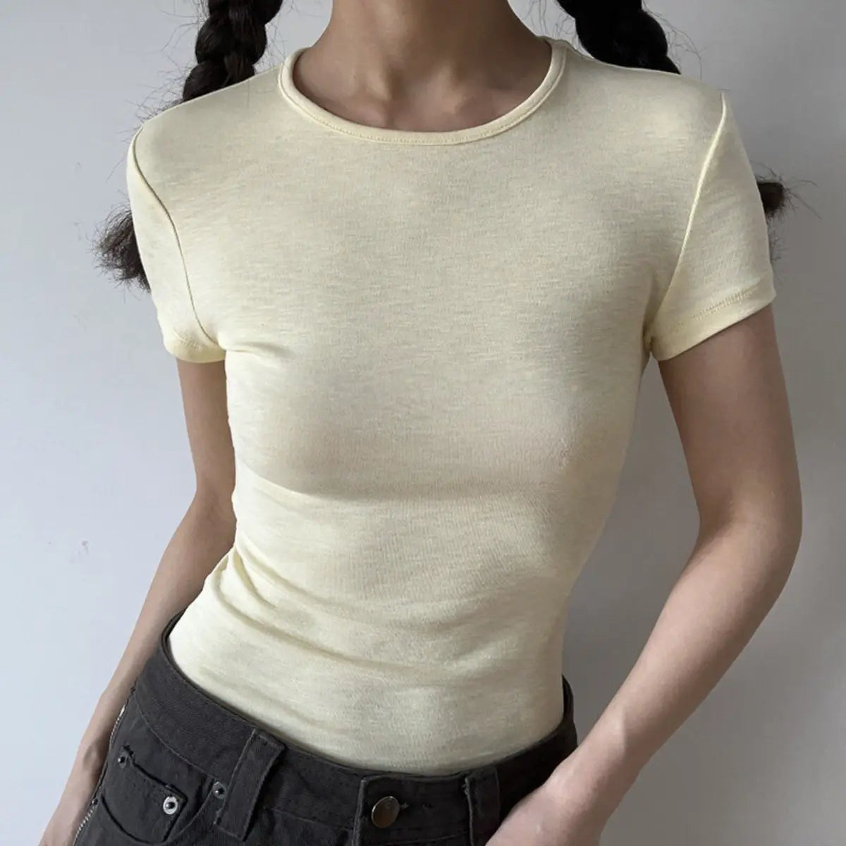 Lifestyle shot of form-fitting cream yellow ribbed crew-neck short-sleeve t-shirt, tucked into jeans