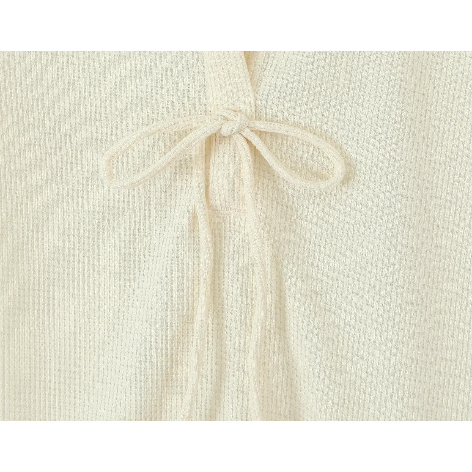 Close‑up shot of front self‑tie knot detail on cream waffle knit dress